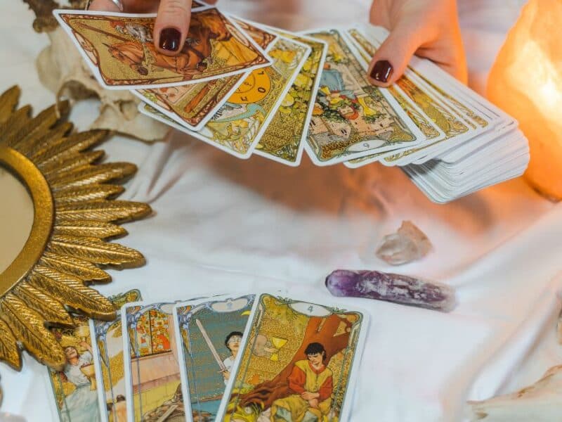 Prriya holding tarot cards with crystals and a golden mirror on a white cloth